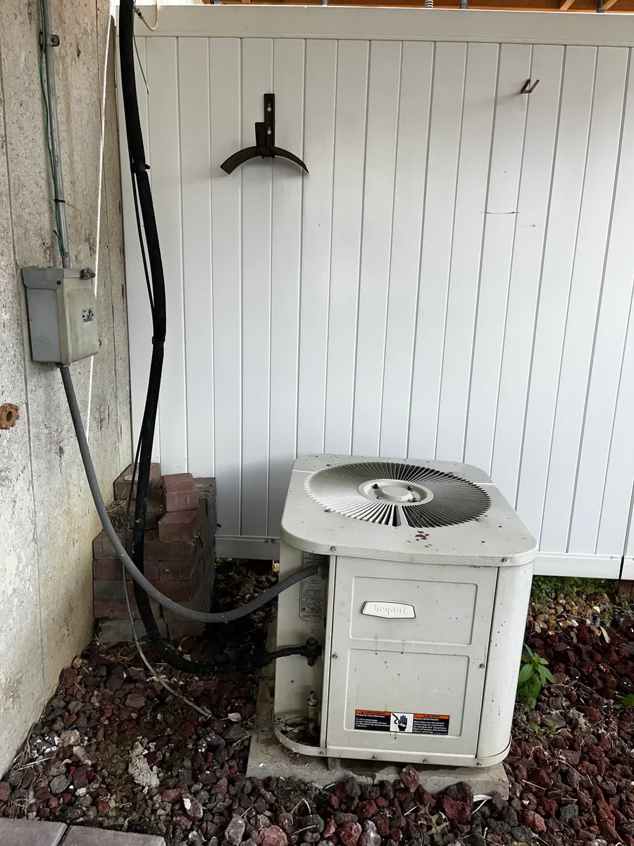 Existing air conditioner beside the covered brick patio before replacement in O'Fallon.